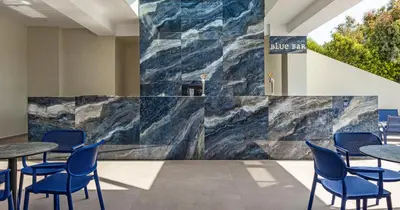 a lobby with blue chairs and a marble wall at Blue Sea Holiday Village in Afantou