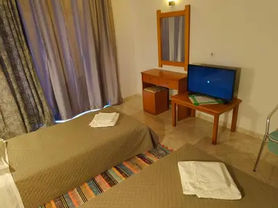 a room with two beds and a desk and a television at Chrysa Apartments in Kolimbia