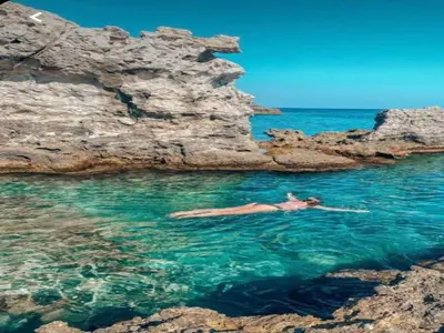 a woman swimming in the water near some rocks at Villa in Rhodes with Infinity Pool in Kalithies