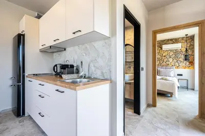 a kitchen with white cabinets and a sink and a bedroom at Pathos SeaSide Suites in Faliraki