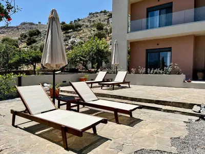 a group of chairs and an umbrella in front of a building at PETRA RESIDENCES IN LINDOS in Líndos