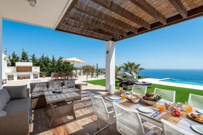 a patio with a table and chairs and the ocean at Diamond Hill Villa in Koskinou