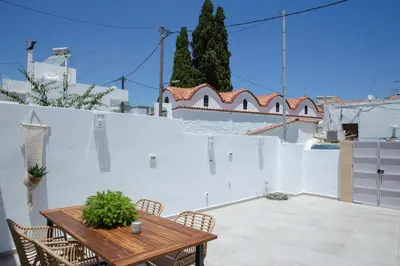 a patio with a wooden table and chairs and a white wall at AENAON in Archangelos