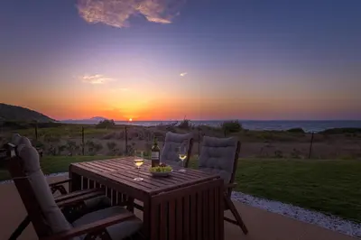 a table with a bottle of wine and two chairs with a sunset at Niva Kamiros Apartments in Kamiros