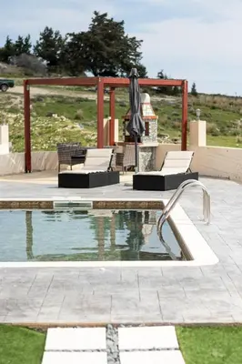 a swimming pool with chairs and an umbrella next to at Kalypso Sea View Villa in Koskinou