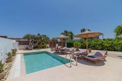 a pool with chairs and umbrellas on a patio at Summer Dream Villa in Afantou