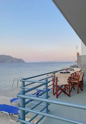 a deck with tables and chairs on the water at Ponente in Symi