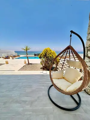 a hanging rattan chair with a view of the ocean at Vaso Beach Front Villa in Ialyssos