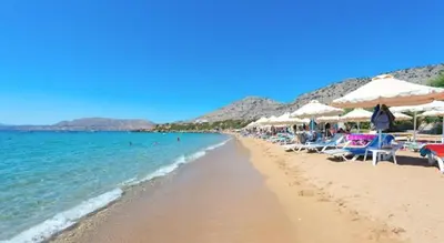 a beach with chairs and umbrellas and the ocean at Karpathios Studios Pefkos in Pefki Rhodes