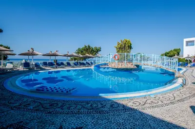 a pool at the beach with chairs and umbrellas at Karpathios Studios Pefkos in Pefki Rhodes