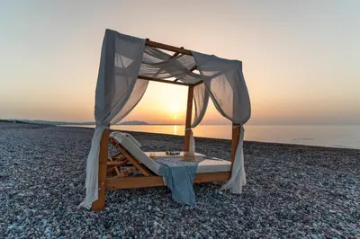 a bed on a beach with the sunset in the background at Aethrion Villas & Suites in Gennadi
