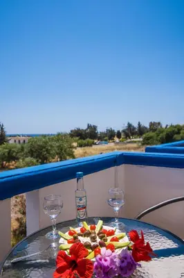 a plate of food on a table with glasses and flowers at Gennadi Sun Apartments 500m from the beach in Gennadi