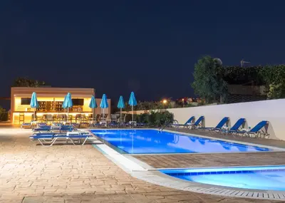 a swimming pool at night with chairs and umbrellas at Amaryllis front beach hotel in Lardos