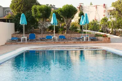 a swimming pool with blue chairs and umbrellas at Amaryllis front beach hotel in Lardos