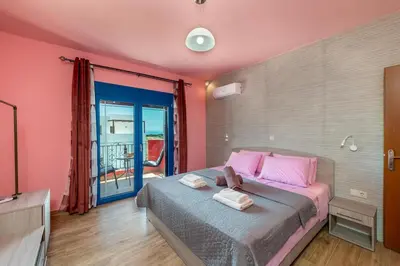 a bedroom with a bed with pink walls and a balcony at Olympia Villa in Gennadi