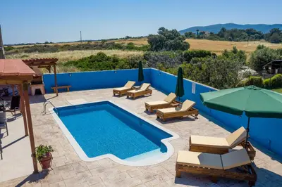 a swimming pool with chairs and a table and an umbrella at Olympia Villa in Gennadi