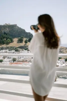 a woman in a white dress taking a picture of a city at Lindos Harmony Suites in Líndos