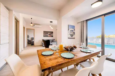 a dining room with a wooden table and white chairs at Villa Angelina Olivestone by Villa Plus in Yennadhion