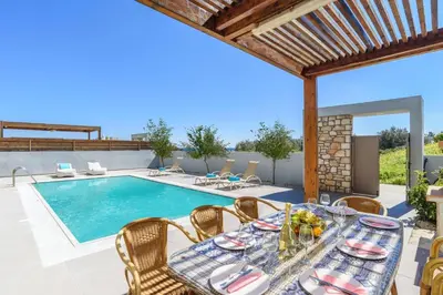 a patio with a table and chairs next to a swimming pool at Villa Angelina Olivestone by Villa Plus in Yennadhion