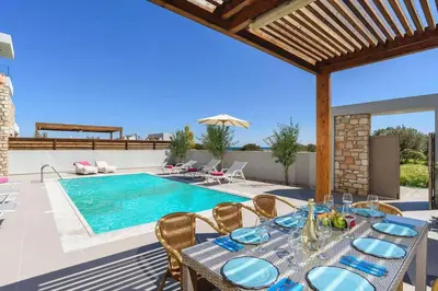 a patio with a table and a swimming pool at Villa Nikos Olivestone by Villa Plus in Yennadhion