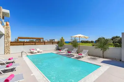 a swimming pool with chairs and an umbrella at Villa Nikos Olivestone by Villa Plus in Yennadhion
