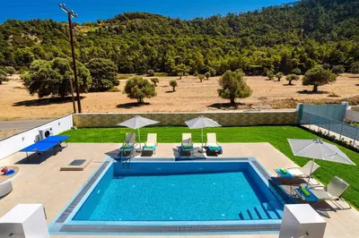 an outdoor swimming pool with chairs and umbrellas at Villa Paleos Evergreen by Villa Plus in Ialyssos