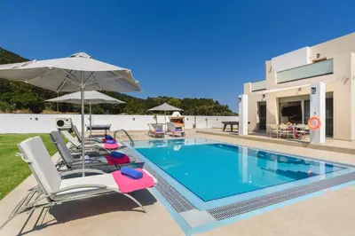 a villa with a swimming pool with chairs and an umbrella at Villa Paleos Hillside by Villa Plus in Ialyssos