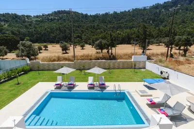 a swimming pool with chairs and umbrellas next to a yard at Villa Paleos Hillside by Villa Plus in Ialyssos