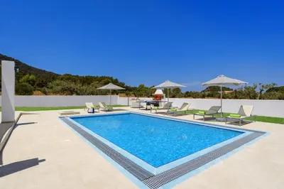 a swimming pool with chairs and umbrellas next to a villa at Villa Paleos Sunset by Villa Plus in Ialyssos