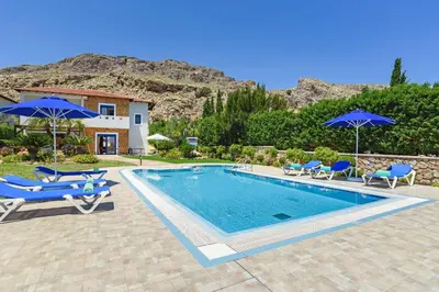 a swimming pool with blue chairs and umbrellas at Villa Clive by Villa Plus in Líndos