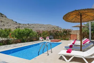 a swimming pool with lounge chairs and an umbrella at Villa Maya by Villa Plus in Pefki Rhodes