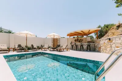 a pool with chairs and umbrellas next to a house at Stavlos Luxury Stone House in Ialyssos
