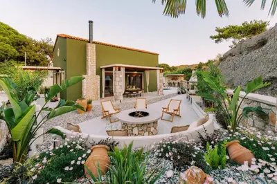 a garden with a table and chairs and a building at Stavlos Luxury Stone House in Ialyssos