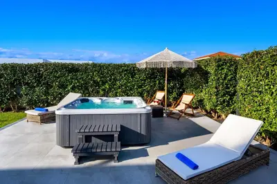 a patio with a hot tub and chairs and an umbrella at Rhodes Villa Billys in Asgourou