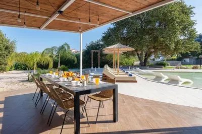 a dining table with chairs and an umbrella on a patio at Hamilton Grand Villa in Koskinou
