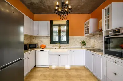 a kitchen with white cabinets and an orange wall at Alki Slow Living Villas in Afantou