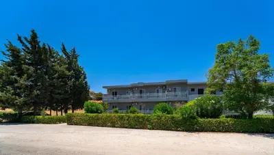 a large building with trees and bushes in front of it at Yiasemi Faliraki Rooms in Faliraki