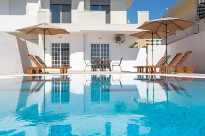 a swimming pool with chairs and umbrellas in front of a house at Anastasia Private Pool Apartment in Afantou