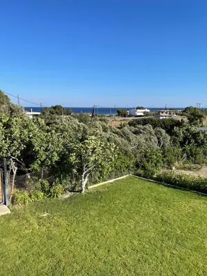a yard with green grass and trees and the ocean at Elena villa-apartments in Asklipiḯon
