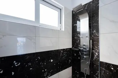 a bathroom with a shower with a window and black tiles at Viviane Paulos Villa in Gennadi