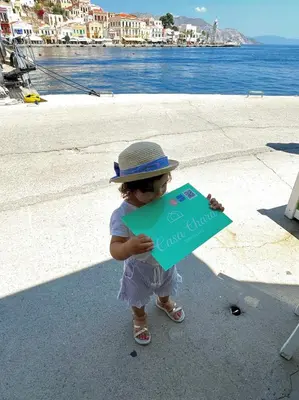 a little girl wearing a hat holding a sign at Casa Chara in Symi