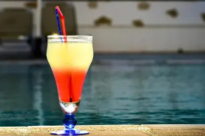 a drink with a red straw sitting next to a pool at Stegna Sunrise Suite Sleeps 4 Pool in Archangelos