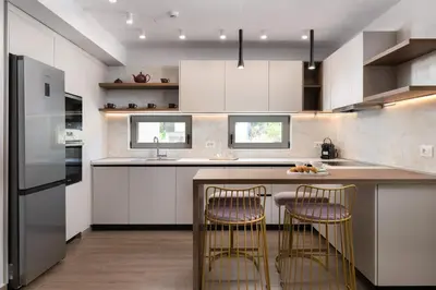 a kitchen with white cabinets and a counter with two bar chairs at ANIMA DEL SOL (BASILICO) in Ixia