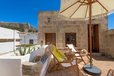 a patio with a couch and an umbrella and chairs at Evangelia's Traditional Villa Lindos in Líndos
