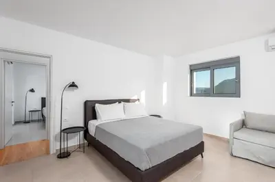 a white bedroom with a bed and a chair at Villa Heather in Kolimbia