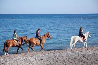 three women are riding horses on the beach at VOULA APARTMENTS in Faliraki