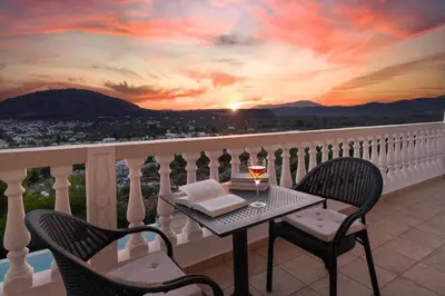 a table with a glass of wine on a balcony with a sunset at Villa Kamos in Archangelos