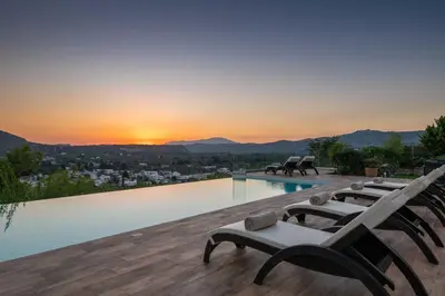 a pool with benches and a view of the sunset at Villa Kamos in Archangelos