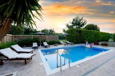 a swimming pool in a backyard with chairs and a table at Island Rodos Pool Suites in Ialyssos