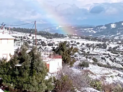 a rainbow over a snow covered field with trees at STONE GUESTHOUSE in Áyios Isídhoros